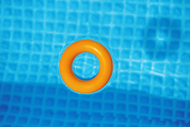 πορτοκαλί φουσκωτό δαχτυλίδι επιπλέουν στην πισίνα στην ηλιόλουστη ημέρα, το top view - Φωτογραφία, εικόνα