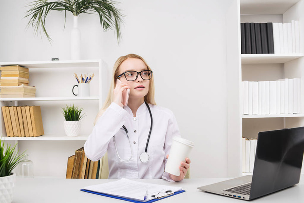 Retrato de una hermosa doctora sonriente mientras habla en el teléfono inteligente y completa una información médica
 - Foto, imagen
