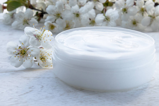 White can, cosmetic cream and cherry flowers on a white background. - Photo, Image