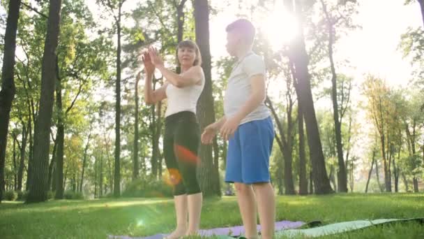 4k slow motion beelden van volwassen vrouw onderwijzen tiener jongen yoga in Park. Fitness lessen oefenen in de natuur - Video
