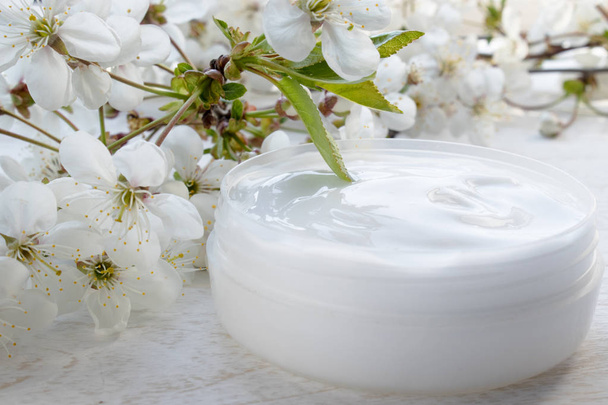 White can, cosmetic cream and cherry flowers on a white background. - Valokuva, kuva