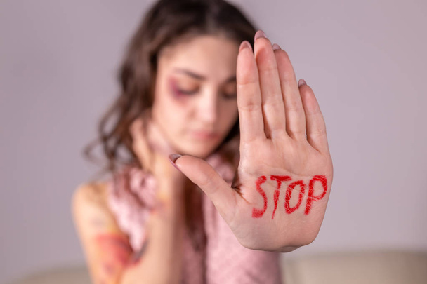 Domestic violence, protesting and people concept - brunette woman expressing denial with STOP on her hand on grey room - Foto, Bild