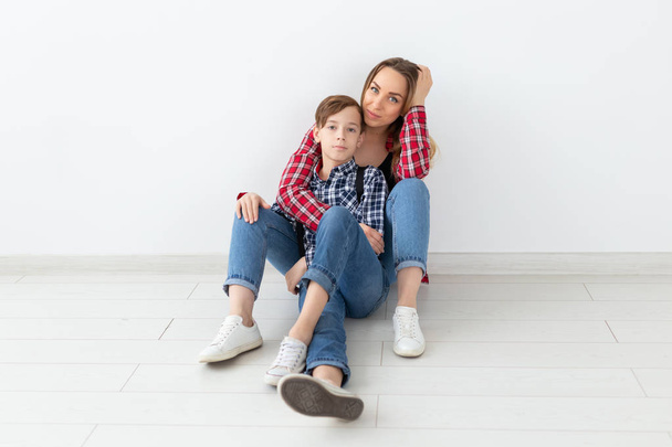 Familie, Mode und Muttertagskonzept - Teenie-Junge umarmt seine Mutter auf weißem Hintergrund - Foto, Bild