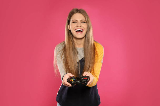 Emotional young woman playing video games with controller on color background - Photo, image