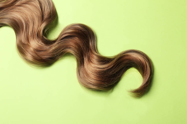 Lock of brown wavy hair on color background, top view - Fotó, kép