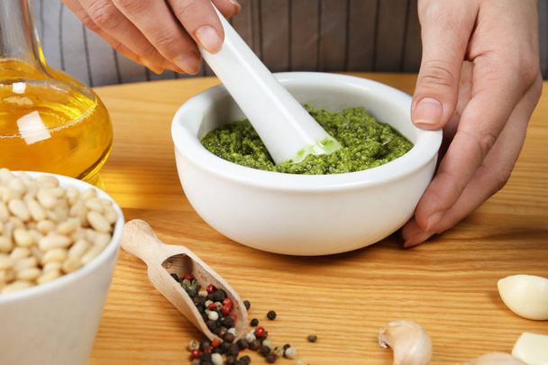 Woman mixing pesto sauce with pestle in mortar at table, closeup - Photo, image