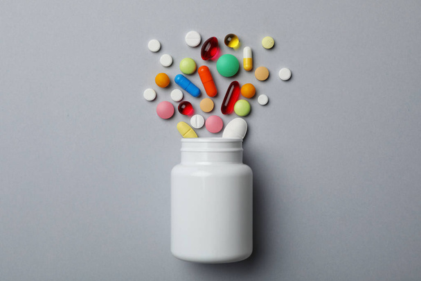 Bottle with different pills on grey background, flat lay - Fotó, kép