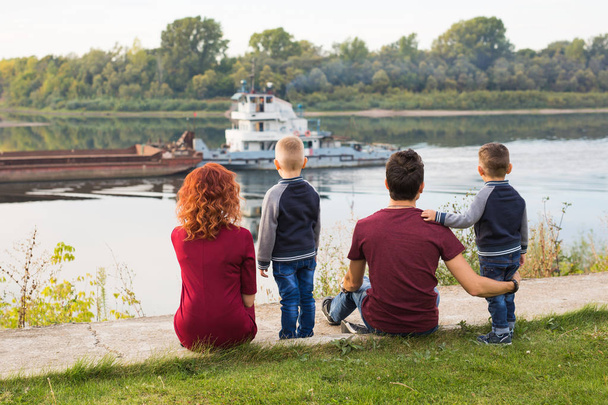 Concept de parentalité, d'enfance et de nature - Famille assise sur le terrain vert et regardant un petit bateau
 - Photo, image