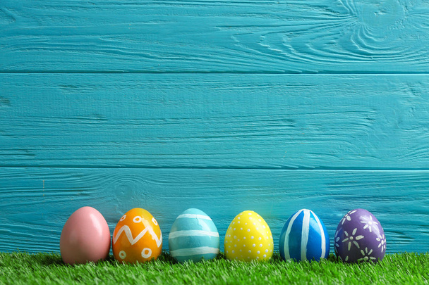 Painted Easter eggs on green grass against wooden background, space for text - Zdjęcie, obraz