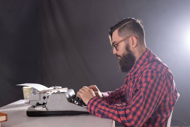 People and technology concept - Side view handsome man with beard working on typewriter over black background - Foto, afbeelding