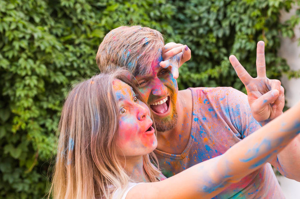 Dovolená, holi a lidé koncept - žena a muž s malovanými obličeji selfie převzetí bush backgrund - Fotografie, Obrázek