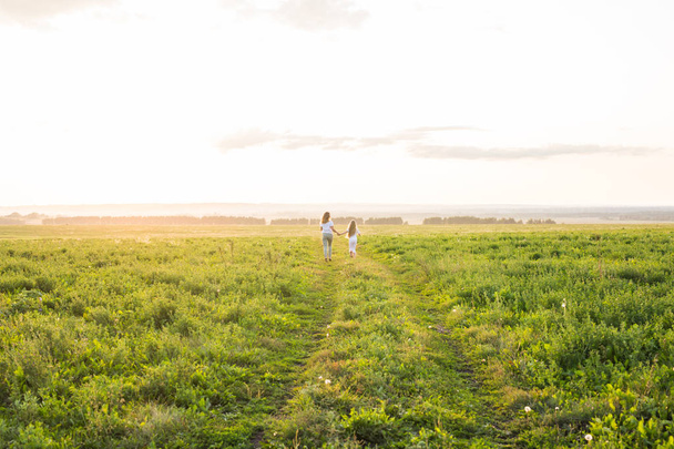 Family, summer and holiday concept - Mother holding her daughters hand running in green field - Фото, изображение