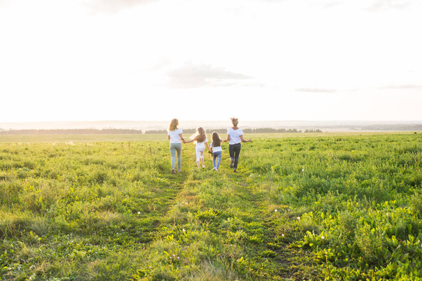 家族、夏休みなどの休暇のコンセプト - 女性と女の子が緑の野原で離れて行くのグループ - 写真・画像