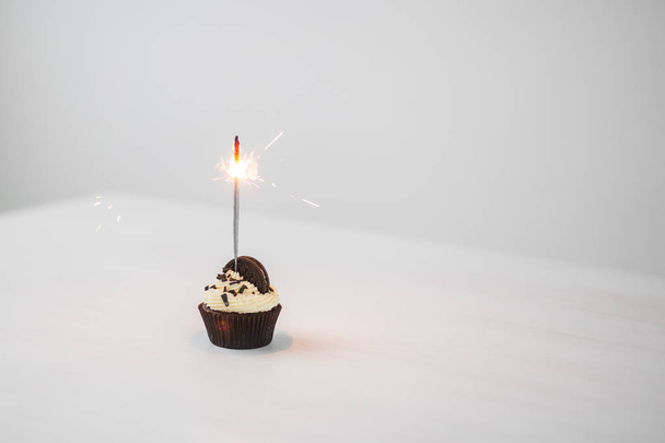 Food and holiday concept - Birthday cupcake with sparkler over white background with copy space - Foto, Imagem