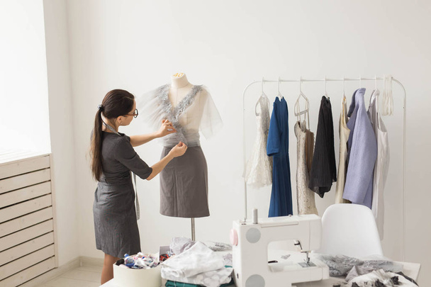 Naaister, kleermaker, mode en showroom concept - zijaanzicht van vrouwelijke mode-ontwerpster meten van materialen op etalagepop in kantoor - Foto, afbeelding