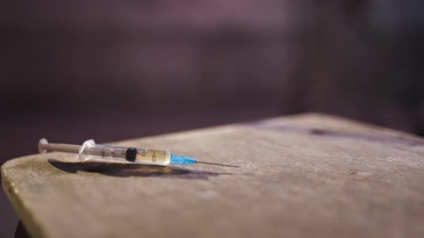 Syringe close up on table with a drug addiction redhead caucasian white young woman in the background sitting and walking away wearing black sweater, skirt and chocker - Footage, Video