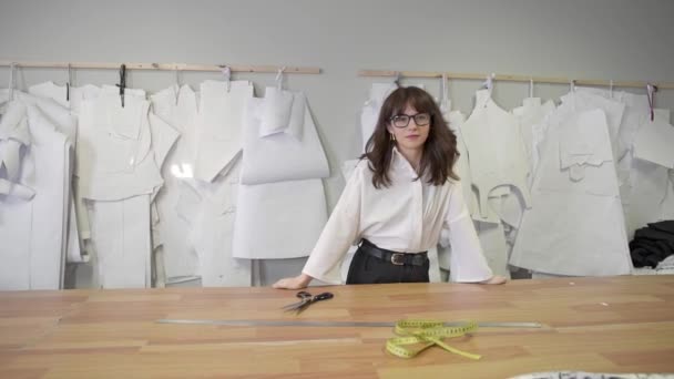 Female fashion designer smiling standing on background of paper patterns - Кадри, відео