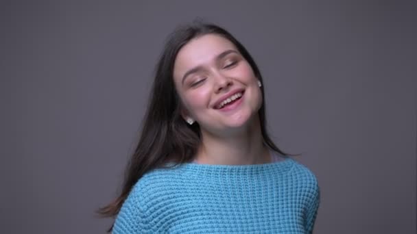 Closeup shoot of young pretty brunette female dancing with joy being relaxed in front of the camera with background isolated on gray - Filmati, video