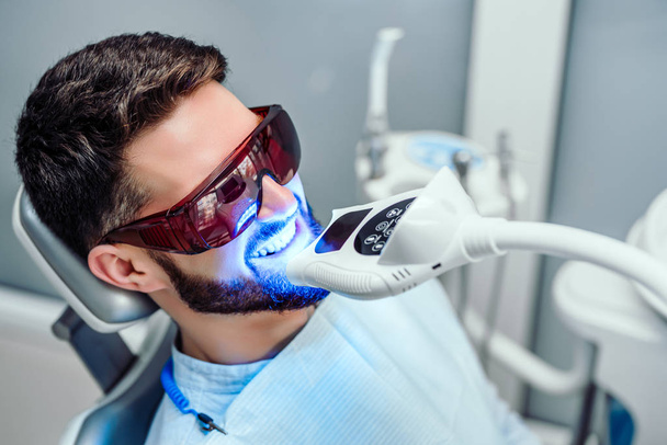 Dentist starting teeth whitening procedure with young man. - Fotoğraf, Görsel
