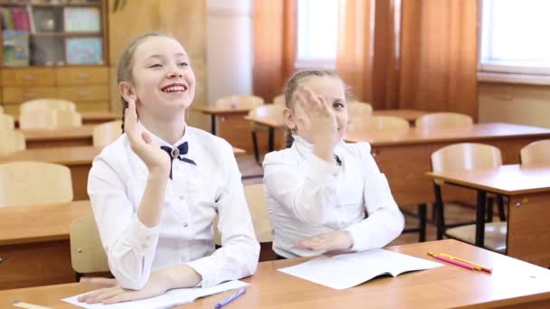 女子高生は先生の質問に答えるために手を上げる。ティーンエイジャーの女子高生の2人の女の子がテーブルに座って、一人の生徒が先生の質問に答えるために手を上げ、2番目の女の子はレッスンの主題を知っています - 映像、動画