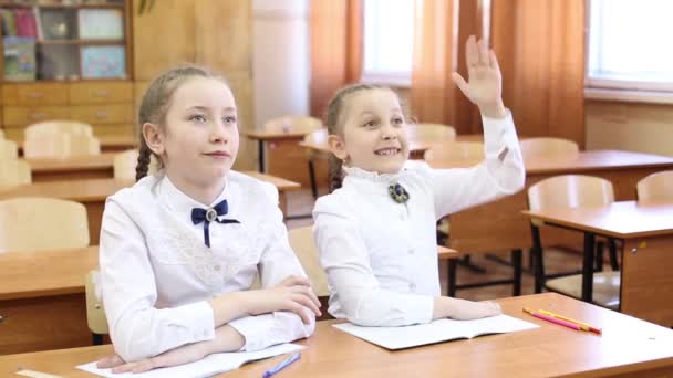 Uczennica podnosi rękę, aby odpowiedzieć na pytanie nauczyciela. Dwie dziewczyny uczennicy nastolatek siedzą przy stole, jeden uczeń podnosi rękę, aby odpowiedzieć na pytanie nauczyciela druga dziewczyna zna temat lekcji lekcji - Materiał filmowy, wideo