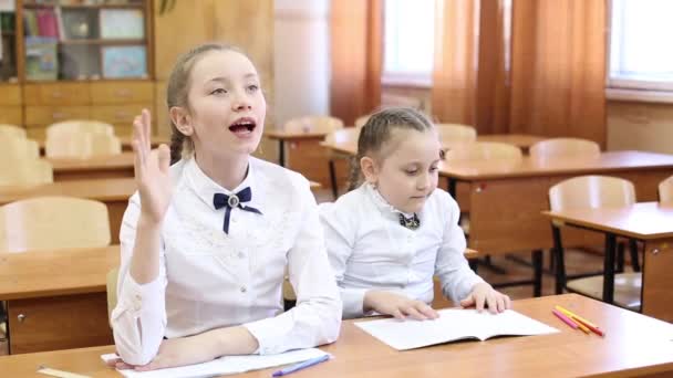 Iskoláslány felemeli a kezét, hogy válaszoljon a tanár kérdésére két lány egy tinédzser iskolás ül az asztalnál, egy diák emeli a kezét, hogy válaszoljon a tanár kérdésére, a második lány tudja, a tárgya a leckét lecke. - Felvétel, videó