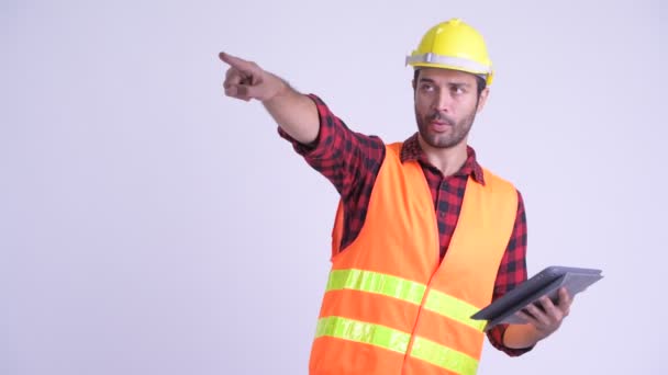 Handsome bearded Persian man construction worker directing while using digital tablet - Felvétel, videó