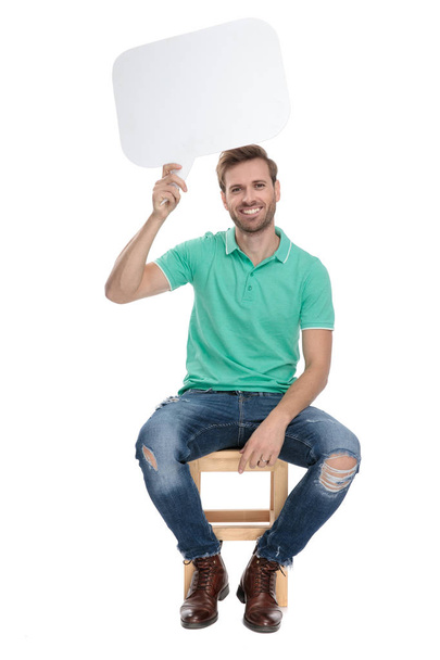 zittende casual man houdt een lege Talk Bubble - Foto, afbeelding