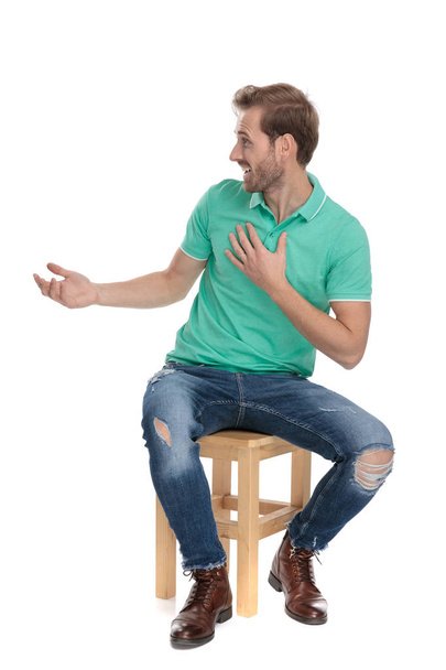 Сидящий случайный парень в зеленой рубашке поло выглядит изумленным
 - Фото, изображение