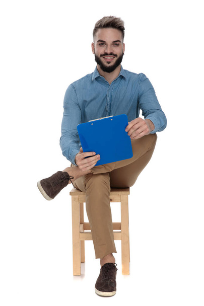 casual man sitting with clipboard in hand and legs crossed - Φωτογραφία, εικόνα