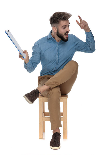 sentado atractivo hombre gritando con un portapapeles en la mano
 - Foto, imagen