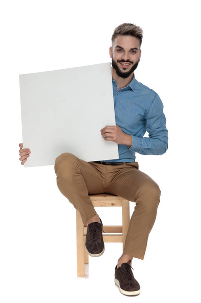 seated smiling man presenting a blank billboard - 写真・画像