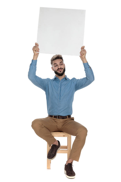 καθισμένος ηλίθιος άνθρωπος κρατά κενή αφίσα στον αέρα - Φωτογραφία, εικόνα