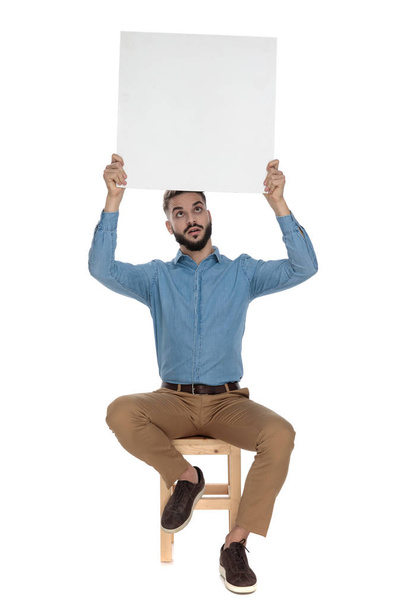 seated goofy man holds blank billboard up in the air - Fotoğraf, Görsel