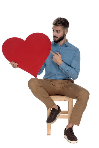 сидить цікавий чоловік, вказуючи пальцем на червоне серце
 - Фото, зображення