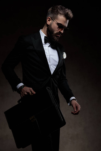 Eleganter Mann im Smoking spaziert mit Aktentasche und blickt nach unten - Foto, Bild