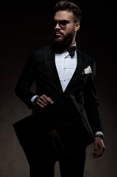 hombre elegante en esmoquin sosteniendo un maletín y mira hacia otro lado
 - Foto, Imagen