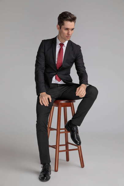 сидящий успешный человек, отводящий взгляд с руками на коленях
 - Фото, изображение