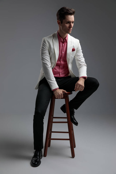 hombre de negocios sentado en traje mirando hacia otro lado con el brazo en la pierna
 - Foto, imagen