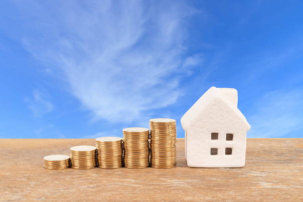 Модельный дом и стопка монет на фоне голубого неба ипотечного сбережения
 - Фото, изображение