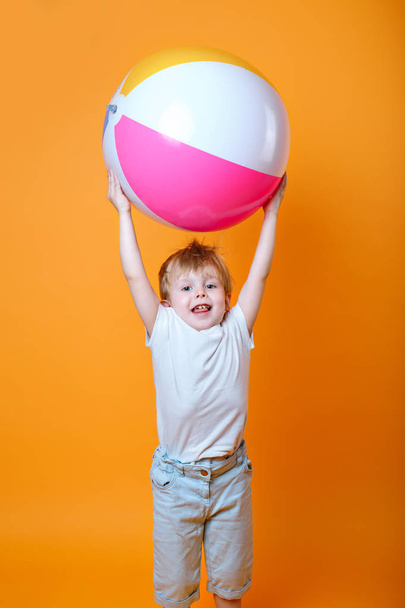 Cute Llttle boy in swimming shorts holding a beach ball on orange background - Fotoğraf, Görsel