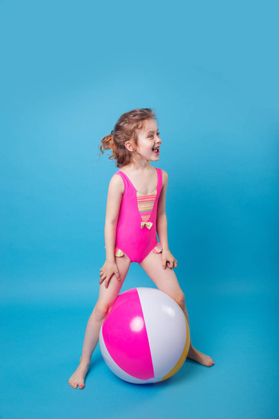 Cute little girl in swimsuit with big inflatable ball on blue background - Valokuva, kuva
