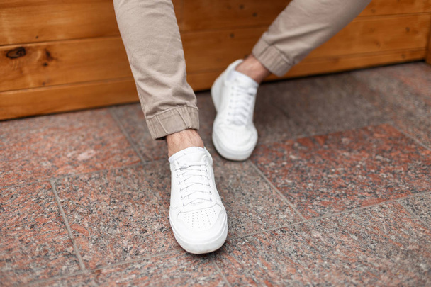 Fashionable men's white leather sneakers. Stylish men's shoes. Casual design. Close-up of male legs. - Photo, Image