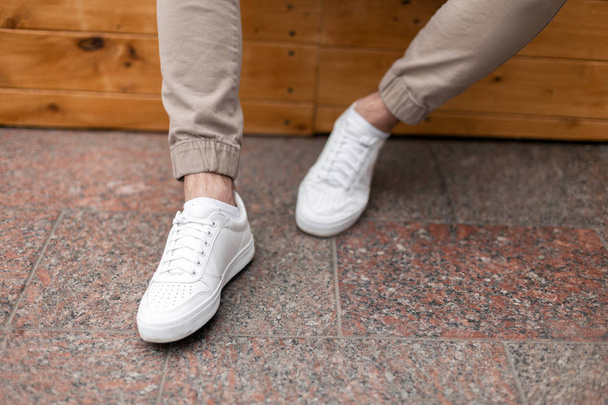 Men's legs in leather fashion white sneakers in stylish beige pants. Trendy casual outfit. Details of everyday look. Street fashion. Close-up. - Photo, Image