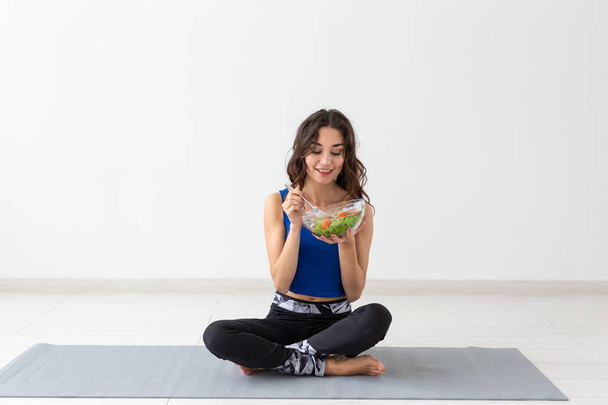 Zdravý životní styl, lidé a sport koncept - jóga žena s miskou zeleninový salát po tréninku nad bílým pozadím - Fotografie, Obrázek