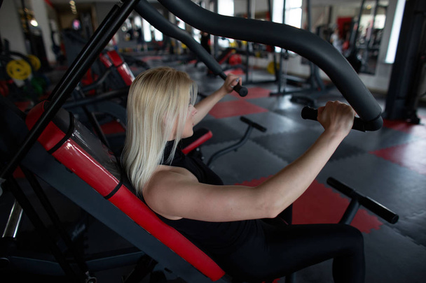 Vue latérale d'une jeune femme sportive en tenue de sport au gymnase. Fille effectue des exercices triceps dans un studio de fitness
. - Photo, image