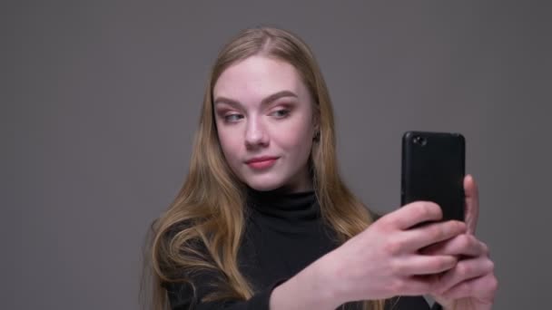 Closeup portrait of young attractive brunette female taking selfies on the phone with background isolated on gray - Metraje, vídeo