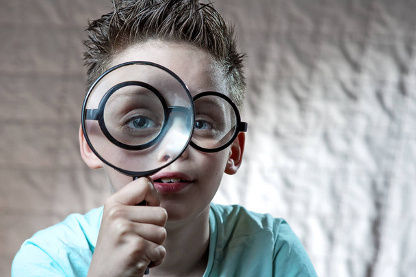 boy in a light t-shirt and glasses looking into a large magnifying glass - Foto, Imagem