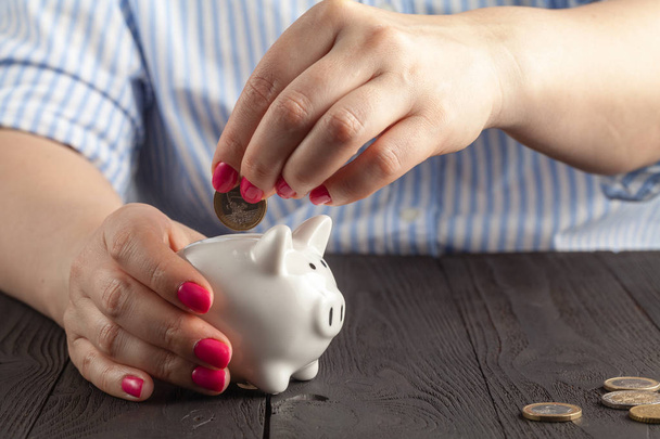 concepto de ahorro, alcancía blanca con la mano femenina humana insertar moneda dentro
 - Foto, imagen