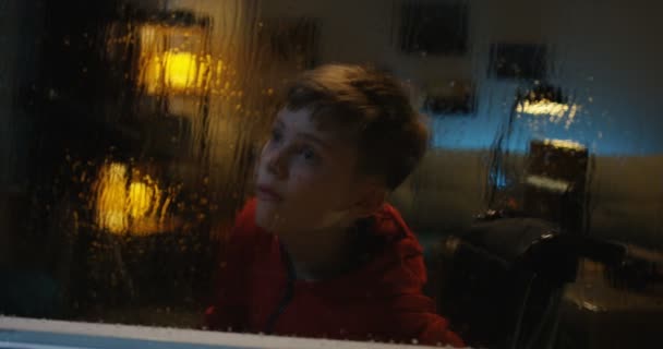 Chłopiec z wózkiem inwalidzkim obserwujący burzę z pokoju - Materiał filmowy, wideo